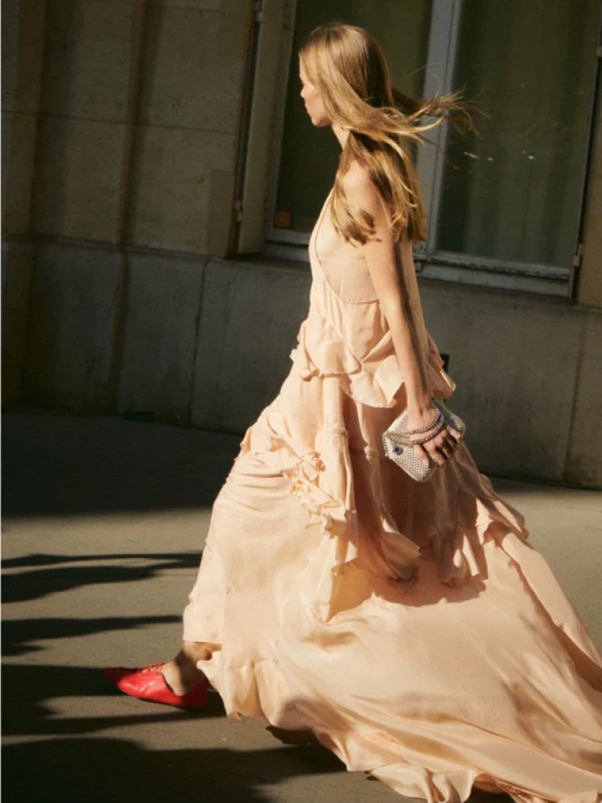 Woman wearing a peach coloured dress walking down a street during a sunset